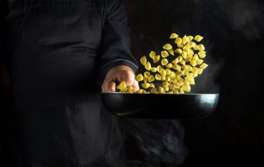 Aşçı sıcak bir tavada makarnadan kahvaltı hazırlar. Sağlıklı vejetaryen yemeği gibi gösterişsiz bir konsept. Siyah arka planda ücretsiz reklam alanı.