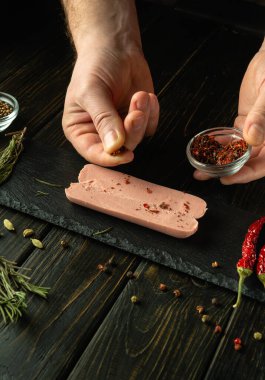 Mutfak masasında bir şefin elleriyle aromatik sosis pişirmek. Izgaradan önce çiğ sosis kesmek için baharat ekliyorum. Reklam için boş alan