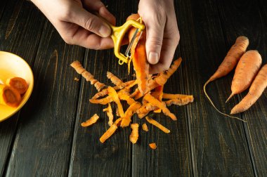 Bir aşçı sebze yemeği hazırlamak için havuç soyar. Siyah bir masanın üzerinde sebze soyacağı olan bir şefin yakın çekimi..