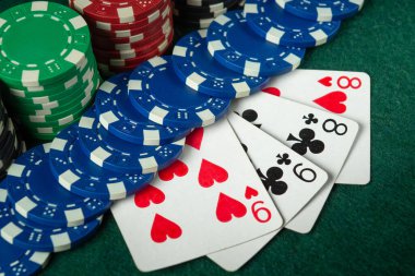 Kumarhanedeki yeşil bir masada iki çift oyun fişi ve kart kombinasyonu bulunur. Heyecan atmosferi dolduruyor.