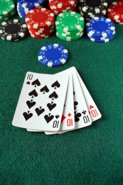 Pokerde kazanan bir el, dört onlu gösteriyor. Kartların etrafında yeşil bir keçeli masa üzerinde çeşitli renkli poker fişleri var. Bu da aktif bir oyun oturumunu gösteriyor..