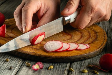 Elleri ustalıkla taze turpları ince ince kesiyor, hatta rahat bir mutfakta ahşap bir kesme tahtasındaki dilimleri bile. Sahne ev yemeklerinin ve sağlıklı hazırlıkların özünü yakalıyor..