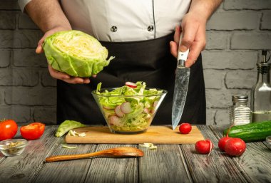 Bir şef sağlıklı bir salata yapmak için lahana ve turplar da dahil olmak üzere taze sebzeleri doğruyor. Sahne ahşap bir kesme tahtası, canlı malzemeler ve kırsal bir masada mutfak aletleri gösteriyor..