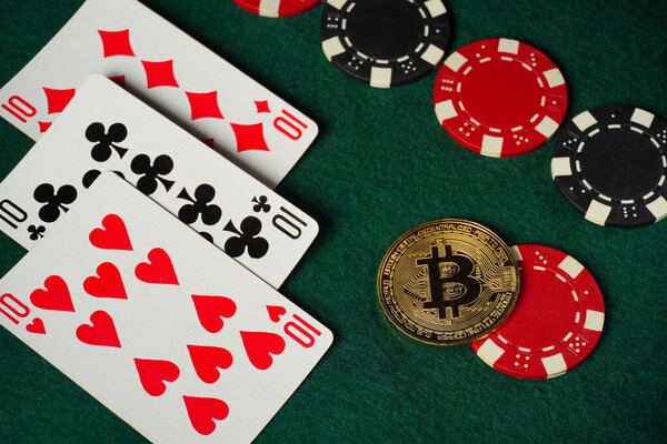Cards featuring three tens are laid out on a green felt surface next to colorful poker chips and Bitcoin, suggesting an exciting evening of poker.