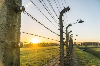 Toplama kampı Auschwitz Birkenau'da, Polonya batımında çevreleyen lambalar ile dikenli tel çit