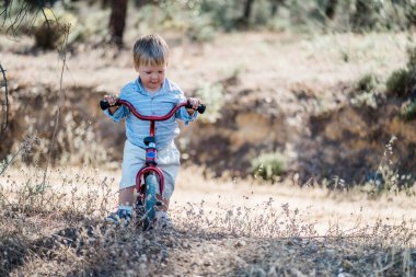 Ormanda küçük bisiklete binen tatlı sarışın çocuk.