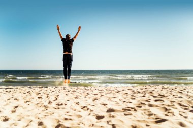 Sahilde elleri havada atlayan bir adam.