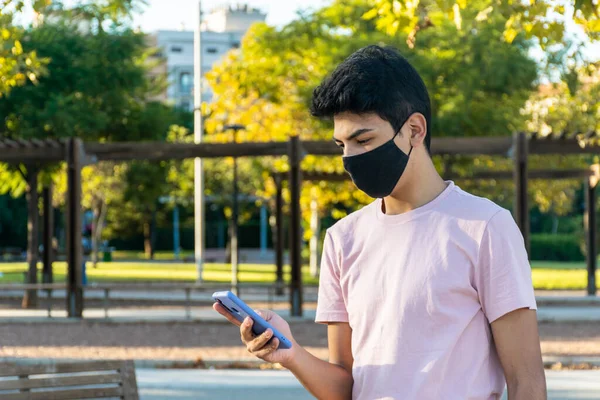 Parkta onun telefonunu kullanarak tıbbi maske takan genç bir adam..