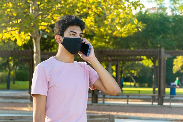 Young man talking on the phone with a medical mask at the park