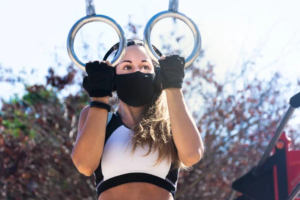 Kulaklıklı ve maskeli atletik genç bir kadın spor salonunda egzersiz yapıyor.