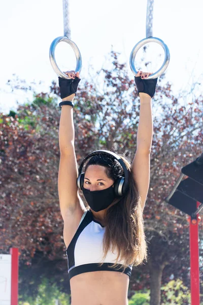 Kulaklıklı ve maskeli atletik genç bir kadın spor salonunda egzersiz yapıyor.