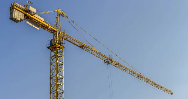 Tower crane at a construction site on a background of blue sky - panorama.