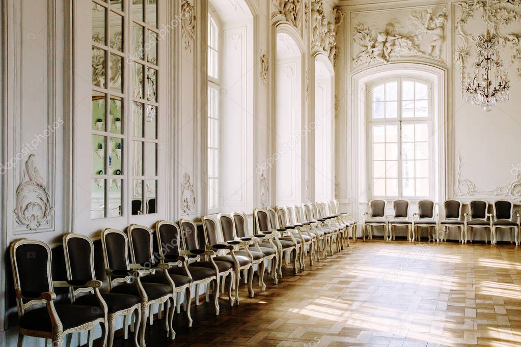 Luxurious light interior in the Baroque style with empty chairs in a row and sunlight.