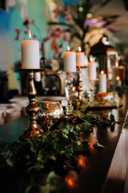 Yanan mumlar ve yeşil sarmaşık yaprakları ile dekore romantik masa ayarı.