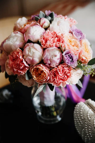 Wedding bouquet of flowers arranged in the vase. Wedding details placed on the table.