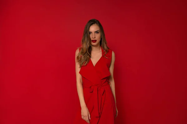 Elegan model Kaukasia mengenakan gaun merah berdiri dengan senyum menawan mengenakan gaun malam . — Stok Foto
