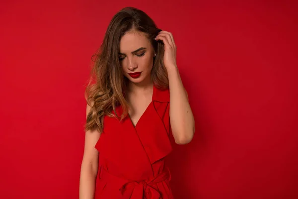 Impresionante mujer europea tocándose el pelo y mirando hacia abajo. Retrato interior de dama romántica en vestido de noche rojo —  Fotos de Stock