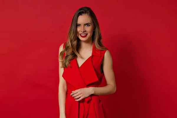 Mujer encantadora sonriente con pelo largo y maquillaje de noche posando sobre fondo rojo y mirando a la cámara — Foto de Stock