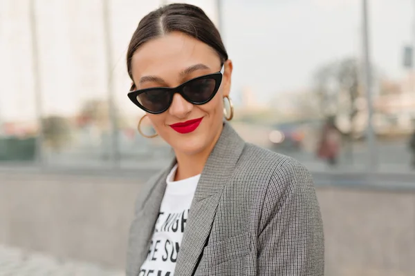 Shot of happy blissful girl with red lips wearing sunglasses, white t-shirt and jacket has fun while listening music — Stok Foto