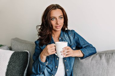 Tabaklanmış teni ve modern rahat evinde bir kanepeüzerinde rahatlatıcı büyük bir gülümseme ile güzel gülümseyen çekici kadın