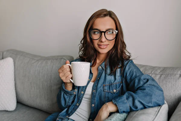 Binnen portret van jonge aantrekkelijke stijlvolle vrouw met gebruinde huid en bruin haar dragen van brillen een blik op venster — Stockfoto