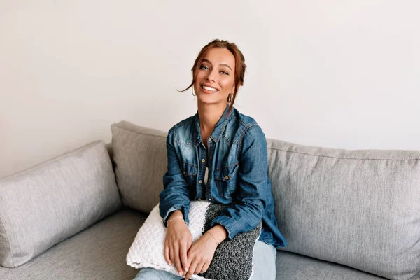 Senyum wanita berambut gelap dengan senyum bahagia duduk di sofa nyaman. Gadis tertawa gembira beristirahat di rumah di akhir pekan . — Stok Foto