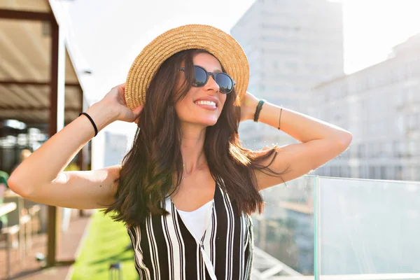 Close-up portrait of lovable caucasian woman in glasses touching her hat on city background in sunlight. — Stock Photo, Image