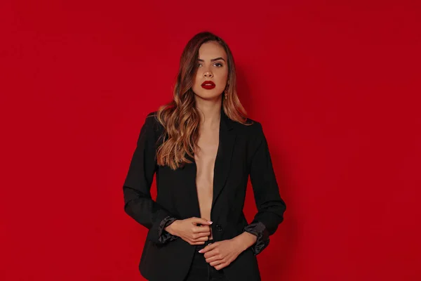 Mujer hermosa caucásica primer plano retrato con maquillaje brillante y labios rojos en traje negro sobre fondo rojo en estudio —  Fotos de Stock