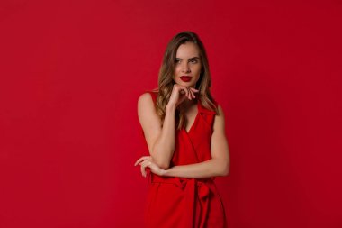 Kırmızı arka plan üzerinde duran zarif elbise inanılmaz ilgilenen kız. Kaygısız beyaz genç kadın gülümsüyor 
