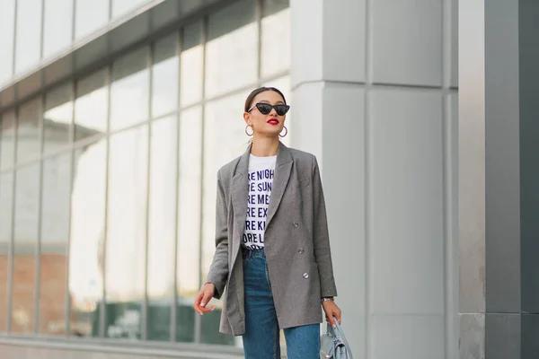 Pengusaha wanita bergaya mengenakan kaos putih, jaket dan celana jeans keluar dari pusat bisnis dan pergi makan siang — Stok Foto