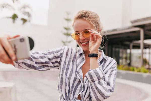 Щаслива чарівна дівчина з світлим волоссям розважається на відкритому повітрі і робить селфі на смартфоні — стокове фото