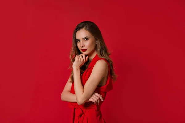 Confident pretty lady wearing red dress with red lips posing to the camera over red background — Stock Photo, Image