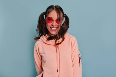 Yuvarlak gözlük ve mavi arka plan üzerinde poz pembe bluz giyen koyu saçlı gülümseyen mutlu kız yakın portresi