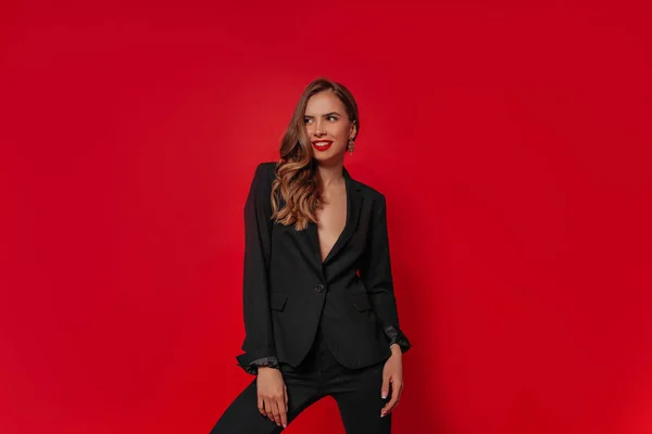 Sonriente modelo elegante atractiva con traje negro con el pelo ondulado y labios rojos posando en el estudio — Foto de Stock