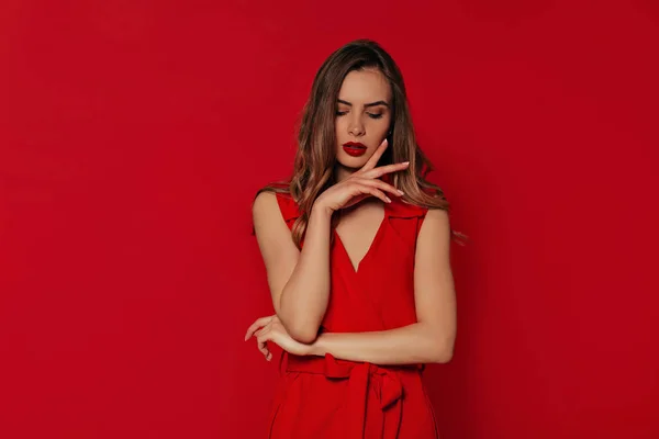 Mujer romántica con estilo en vestido rojo noche posando sobre fondo rojo aislado mientras tiene una sesión de fotos —  Fotos de Stock