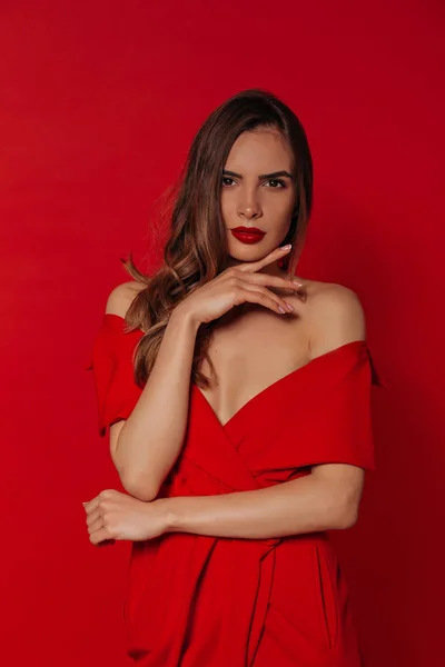 사진 촬영 중 빨간색 배경 위에 세련된 빨간 드레스를 입고 빨간 입술을 가진 자신감있는 현대 아름다운 여성 — 스톡 사진