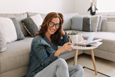Kameraya bakan, dizüstü bilgisayar kullanan, gülümseyen ve çalışan büyüleyici genç kadın.