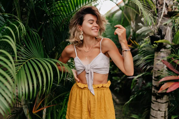 Energetic lovely woman with short hairstyle wearing yellow shorts and top dancing and having fun outside in summer day