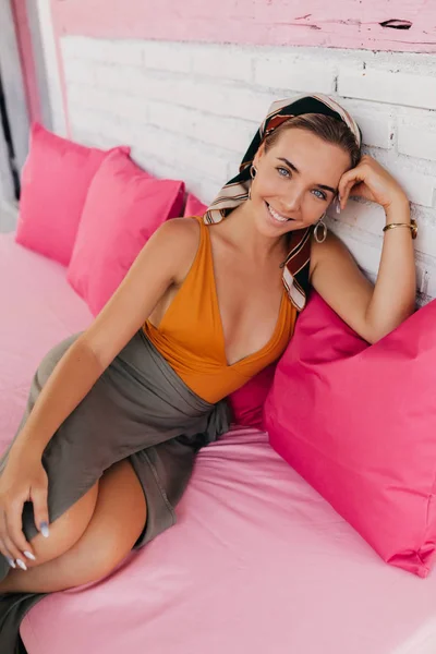身着橙色泳装的笑白种女孩的肖像，在夏天的露台上，在粉红色枕头上喝咖啡，轻松而坐 — 图库照片