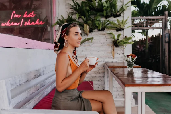 창 옆에 커피 한 잔과 함께 레스토랑에 앉아 행복한 젊은 아가씨의 야외 초상화 — 스톡 사진