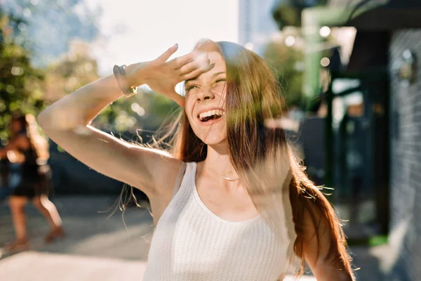 Potret wanita muda yang menggemaskan dengan blus putih dan celana pendek denim bersenang-senang di luar di bawah sinar matahari di kota — Stok Foto