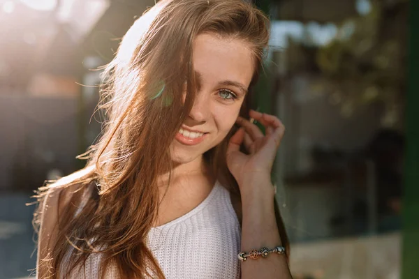 Tutup potret gadis tersenyum bahagia dengan rambut panjang dan mata biru berpose ke kamera di bawah sinar matahari — Stok Foto