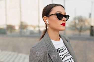 Kendine güvenen modern şık kadın müzik ile iş bölgesinde beyaz t-shirt ve ceket waling giyiyor. 