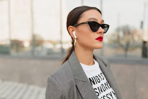 Confident modern stylish woman wearing white t-shirt and jacket waling in business district with music.