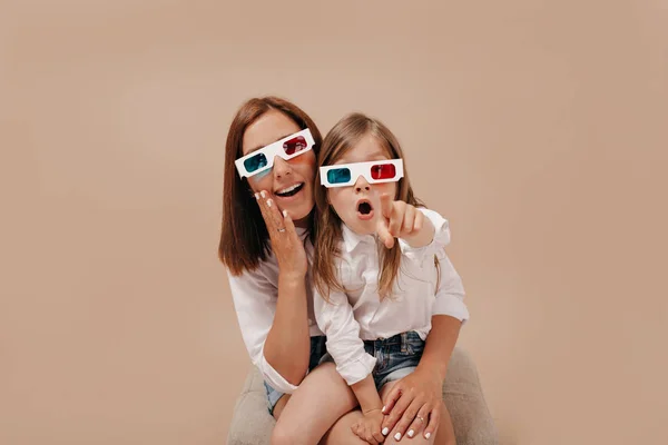 Gadis kecil yang cantik dengan ibu menonton film dengan kacamata 3D dan menunjukkan titik ke kamera — Stok Foto
