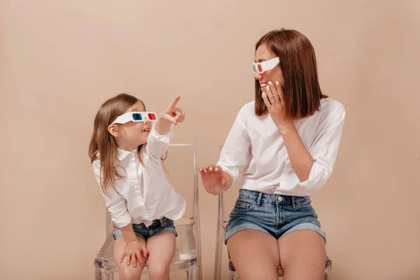 Ibu dan anak saling memandang dan tersenyum dalam kacamata 3D ke kamera di sofa terisolasi pada latar beige . — Stok Foto