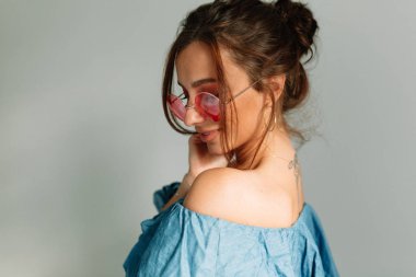 Gri arka plan üzerinde açık bir gülümseme ile aşağı bakarak toplanan koyu saçlı Charming güzel genç kadın