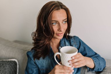 Tabaklanmış deri ile Sevimli sevimli kadın bir fincan çay ile kanepede oturan ve pencereye bakarak 