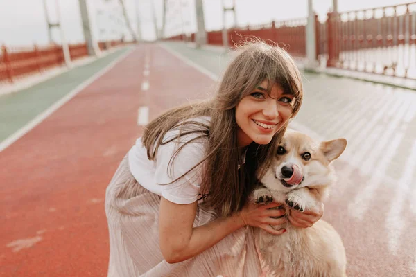 Ramah bahagia kaukasia wanita mengenakan pink rok dan t-shirt putih berpose di kamera dengan anjing kecilnya yang lucu — Stok Foto