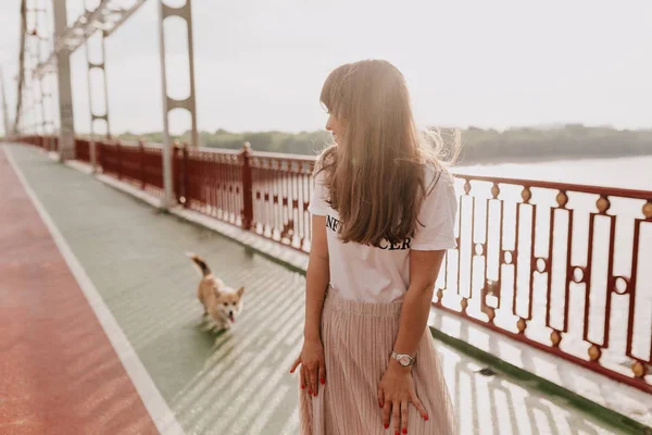 Прекрасна мила жінка в рожевій спідниці та білій футболці, що гуляє в сонячний хороший день зі своїм маленьким собакою — стокове фото